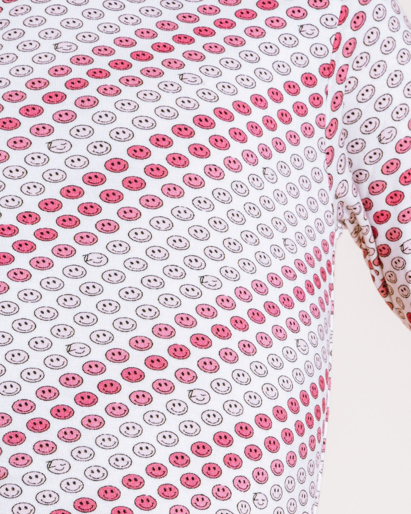 A close-up of a person wearing a long-sleeve top with a repeating red and gray smiley face pattern on a white background, against a plain light background.