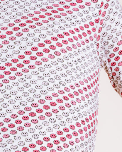 A close-up of a person wearing a long-sleeve top with a repeating red and gray smiley face pattern on a white background, against a plain light background.