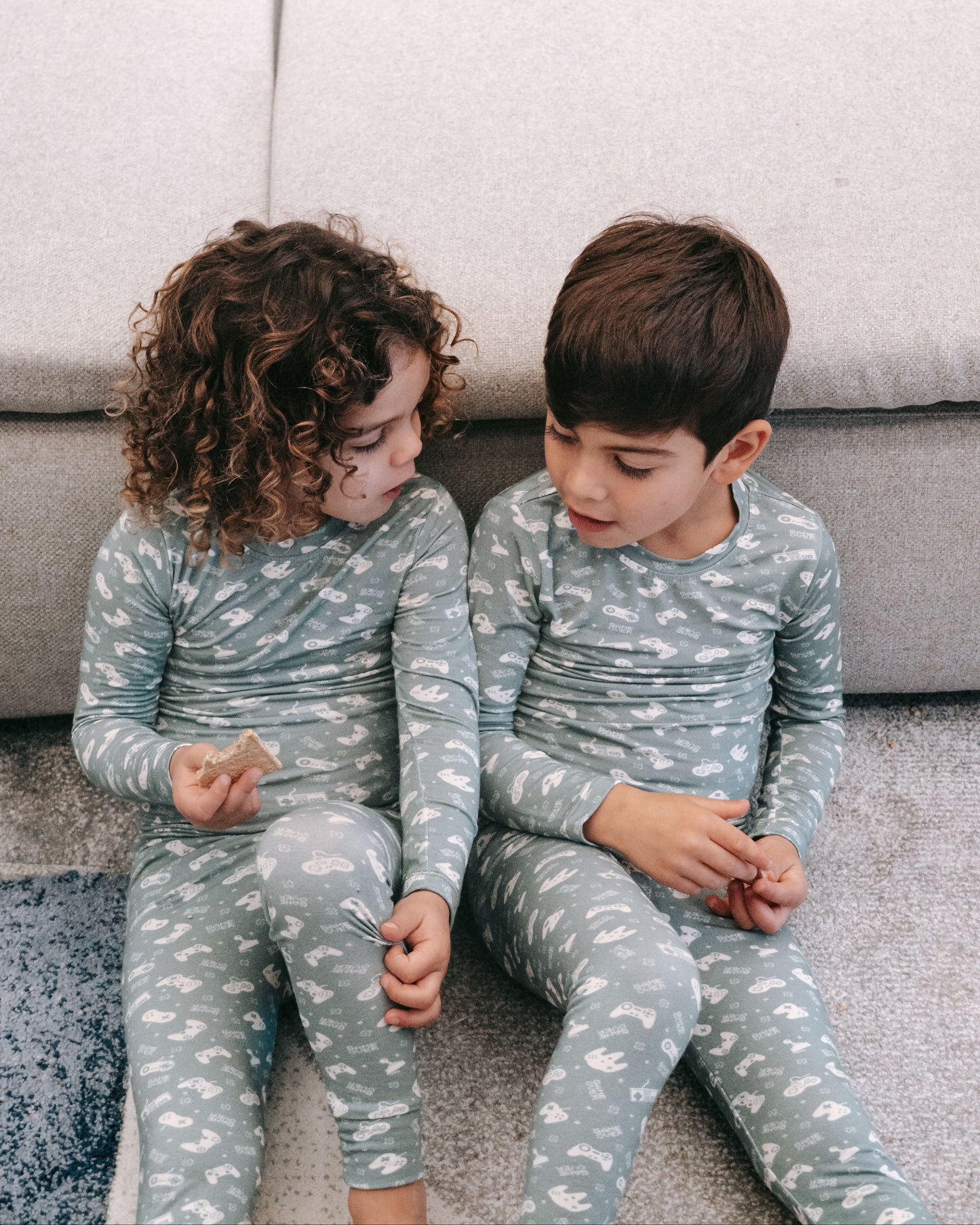 Two children in matching pajamas sitting on a couch.