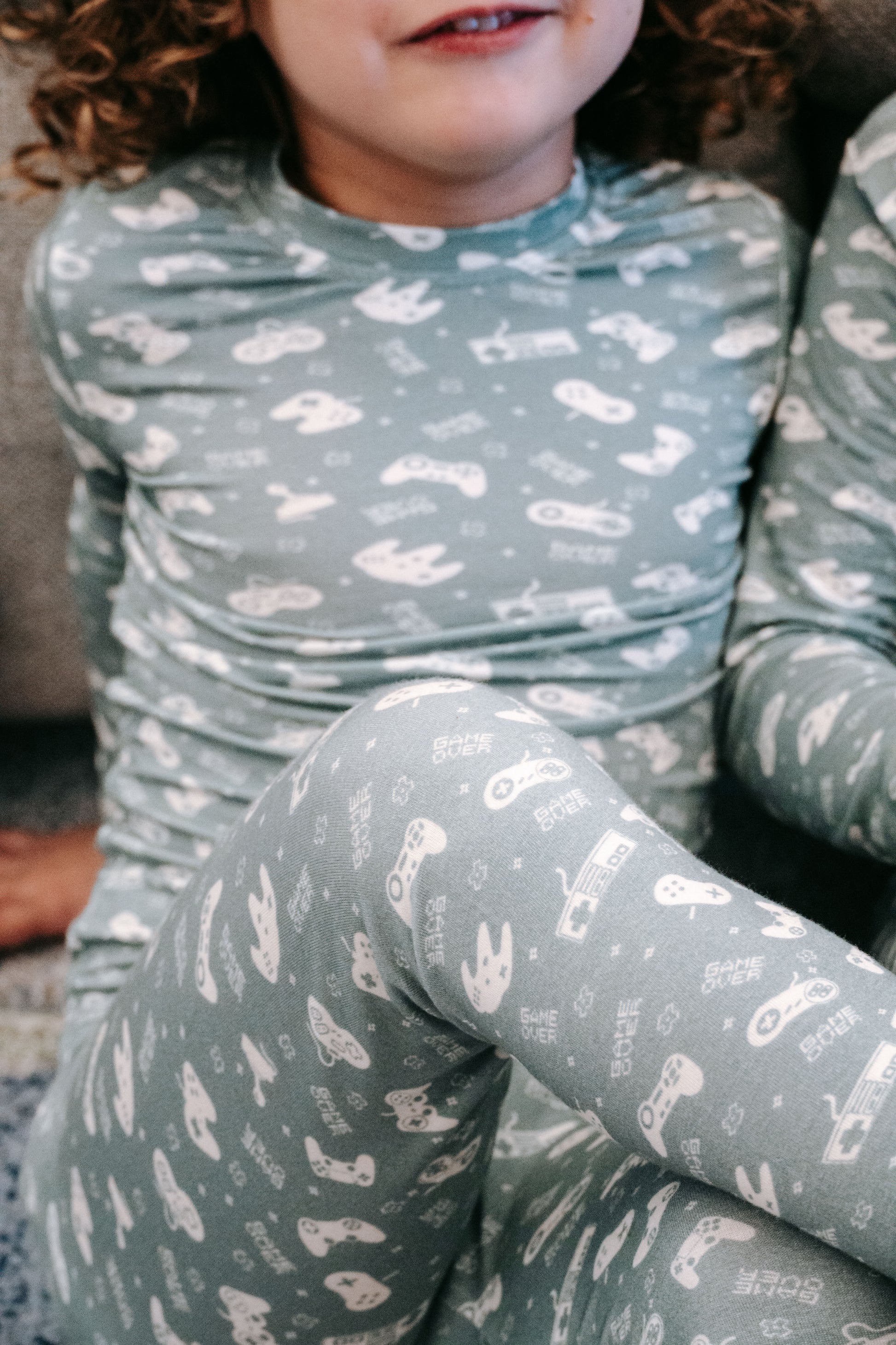 Child wearing a green pajama set with animal prints sitting on a couch.
