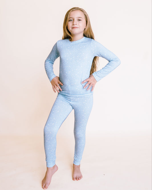 Young girl wearing a light blue long-sleeve shirt and leggings set on a beige background